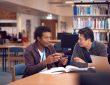 two male adult students talking at table in library