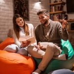 Happy couple smiling and reading book while sitting on lazy bags. Woman holding book. Living room interior.