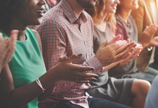 people sitting in chairs clapping at conference