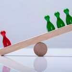 Red And Green Pawns Figures Balancing On Wooden Seesaw