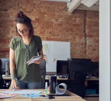 Interior designer or architect in casual wear with messy hairdo making notes while looking at a blueprint