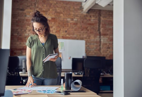 Interior designer or architect in casual wear with messy hairdo making notes while looking at a blueprint