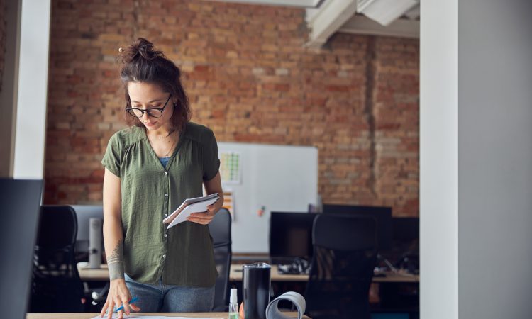 Interior designer or architect in casual wear with messy hairdo making notes while looking at a blueprint