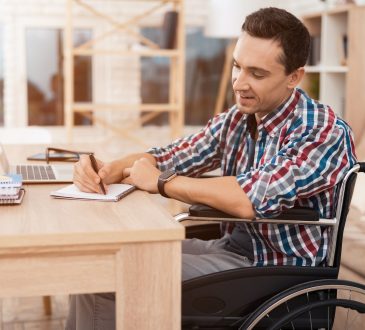 Man sits in a wheelchair at his desk.