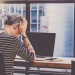 person with head in hands in front of computer