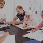 diverse group of people sitting around table listening to instructor