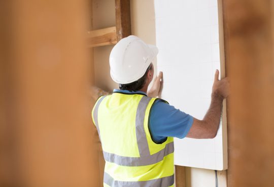 Builder Fitting Insulation Boards Into Roof Of New Home