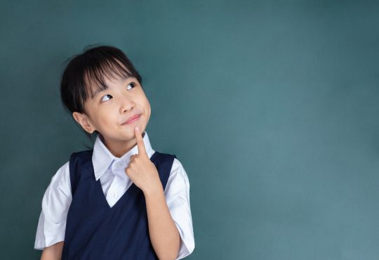 little Girl thinking with finger on chin against green blackboard
