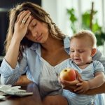 Young mother feeling exhausted while being with her baby and working at home.