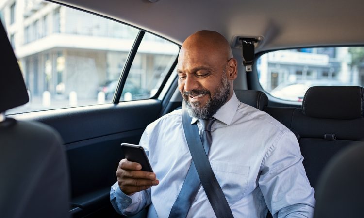 man reading on phone in back of car
