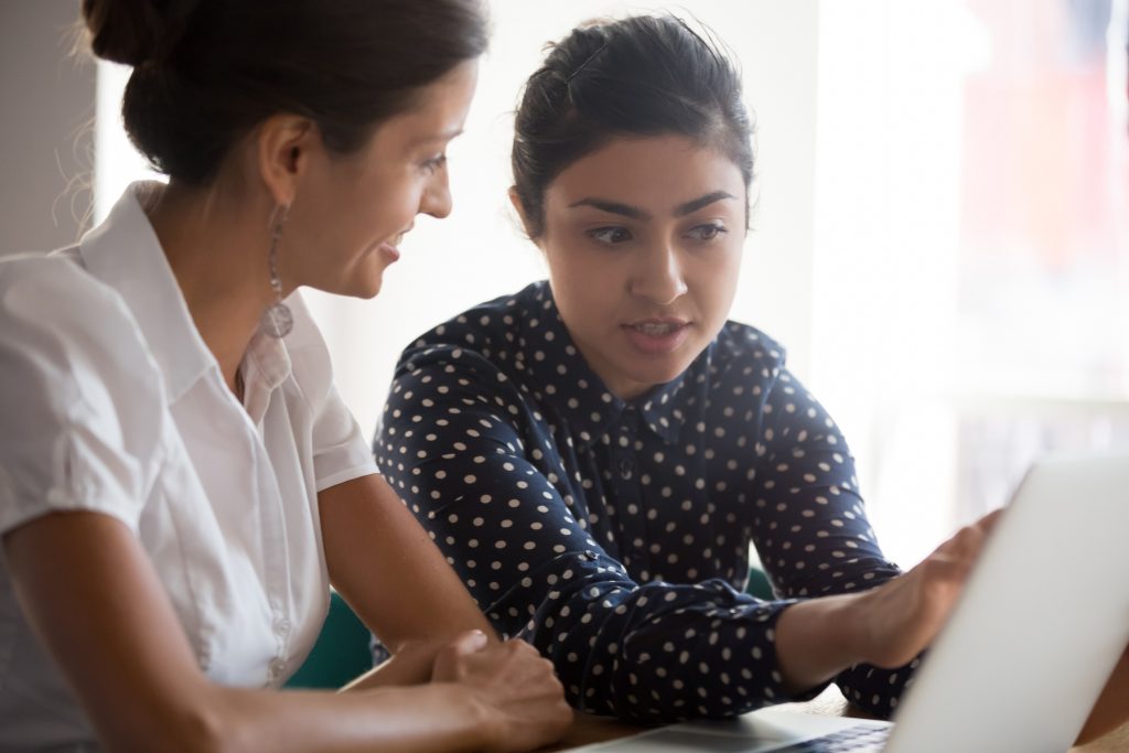 One woman points something out to another woman on laptop screen