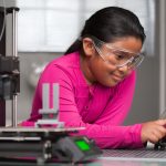 A young student wearing pink is working on a touchscreen making changes to a 3d printed toy in a summer school tech class.