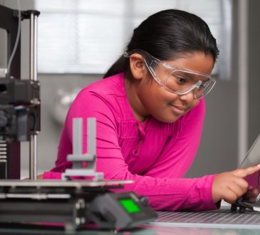 A young student wearing pink is working on a touchscreen making changes to a 3d printed toy in a summer school tech class.