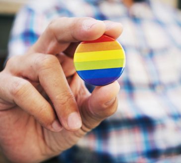 closeup of a young caucasian man outdoors holding a badge patterned with a rainbow flag