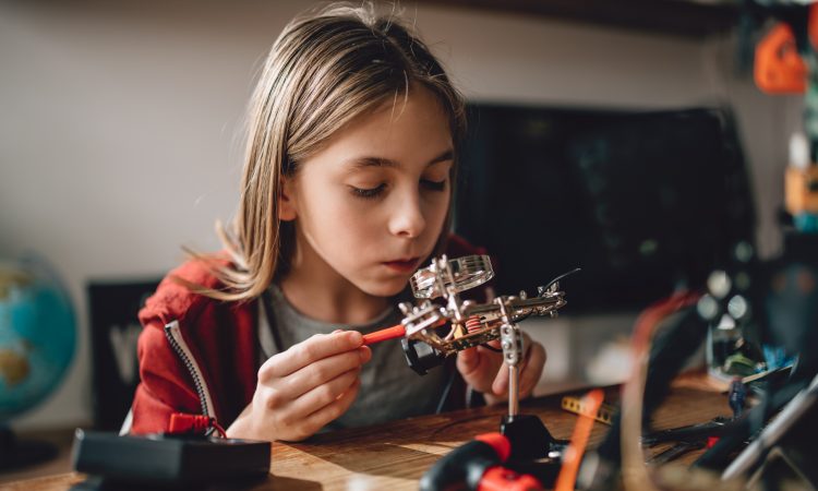 Girl wearing red hoodie looking circuit board throughout magnifying glass at home and building a robot