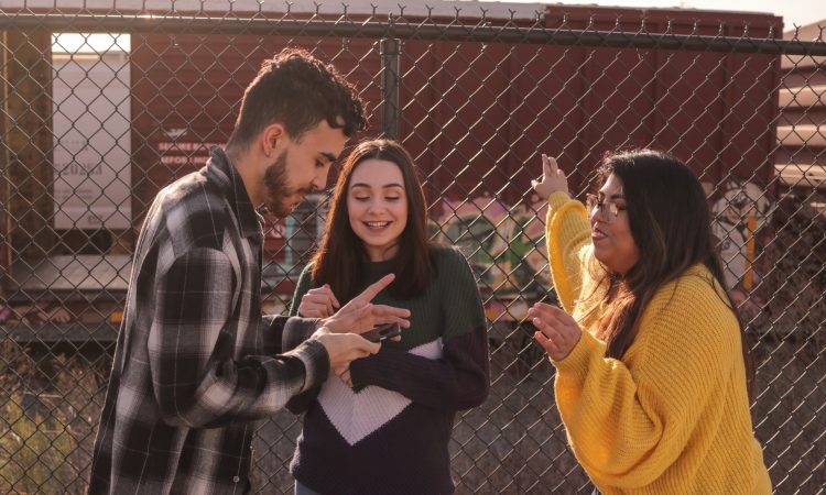 three young people talking by chain link fence