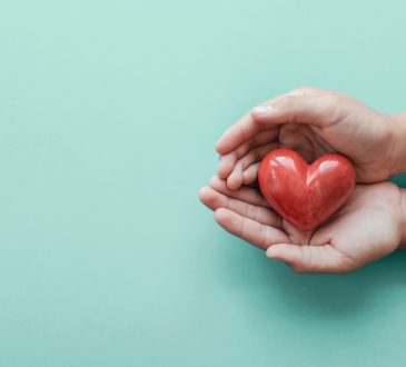 hands holding red heart on blue background