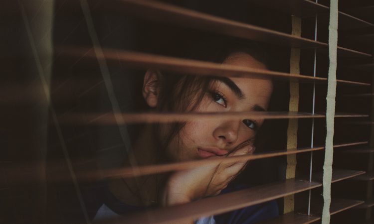 woman looking through blind slats looking worried
