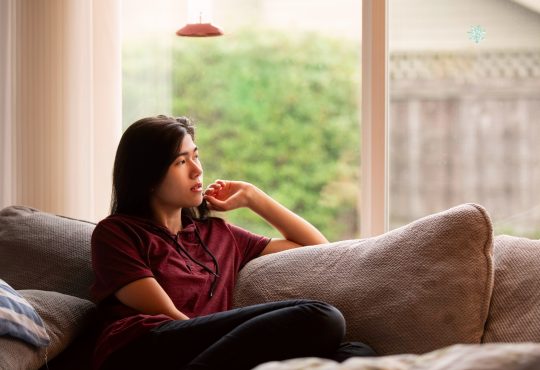 teen sitting on couch looking out window