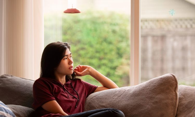teen sitting on couch looking out window