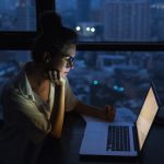 Woman is working with laptop at home during night.