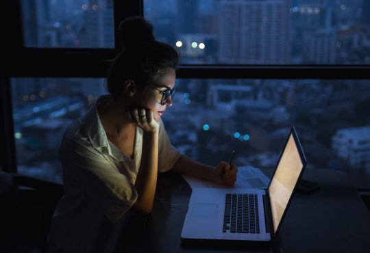 Woman is working with laptop at home during night.