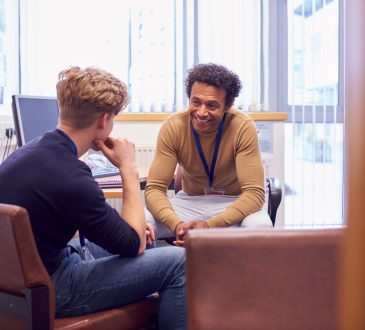 Male College Student Meeting With Campus Counselor Discussing Mental Health Issues