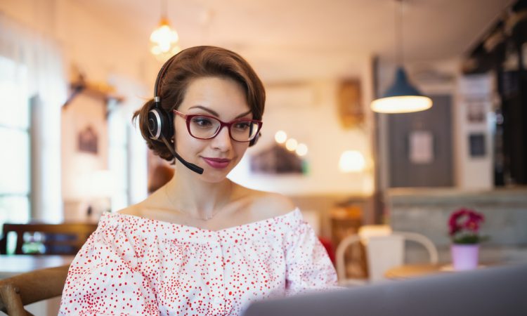 Portrait of young woman with headset and laptop indoors in cafe, working.