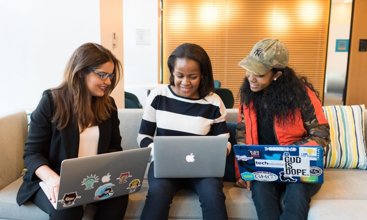 three women using laptops on couch