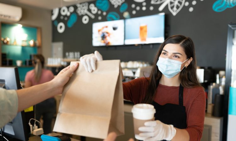 Young female staff giving parcel and coffee to customer at takeaway counter in coffee shop