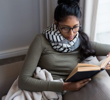Woman reading book by window on sofa at home