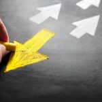 person drawing yellow arrow on chalk board pointing away from white arrows