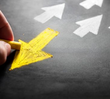 person drawing yellow arrow on chalk board pointing away from white arrows