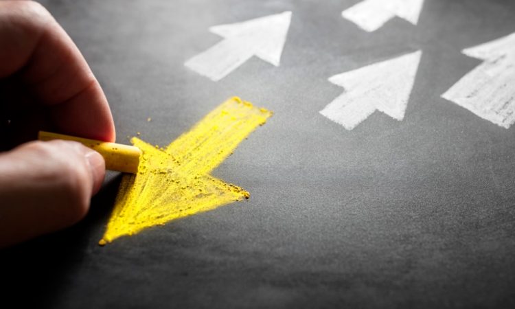 person drawing yellow arrow on chalk board pointing away from white arrows