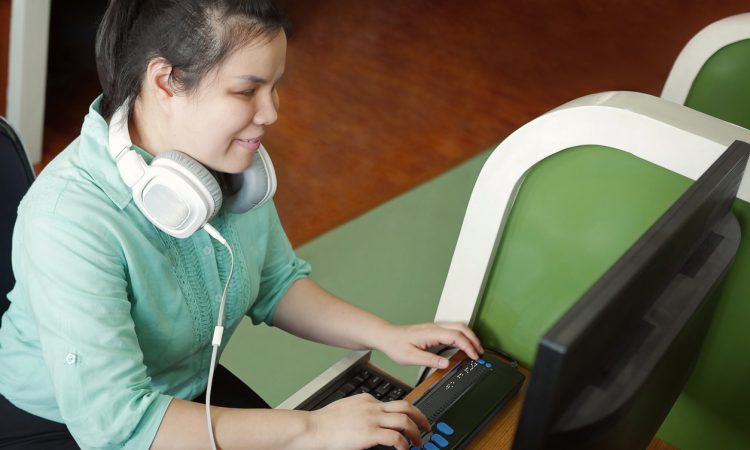Woman with visual impairment wearing headphones using computer with refreshable braille display