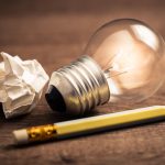 Pencil with glowing light bulb and crumpled paper on wood table