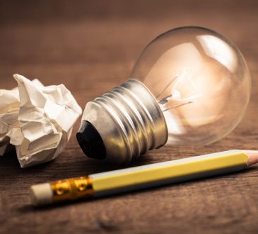 Pencil with glowing light bulb and crumpled paper on wood table