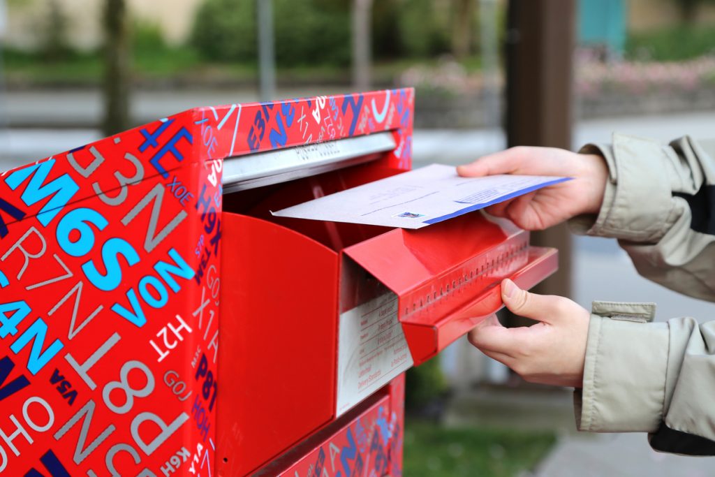 Person mailing letter in red mail box