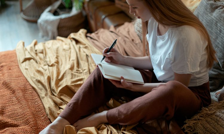 woman writing in journal on bed