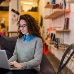 young woman sitting on bench in office working on laptop