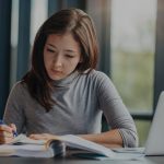 woman writing in notebook in front of laptop