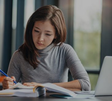 woman writing in notebook in front of laptop