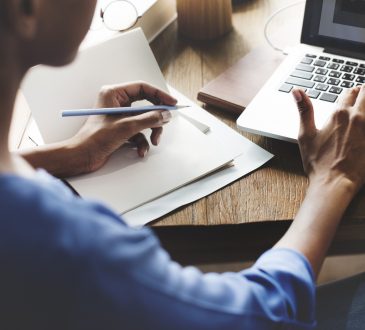 woman holding pencil in one hand with other hand hovering over laptop keyboard