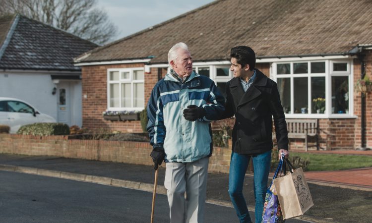 young man helping old man carry groceries