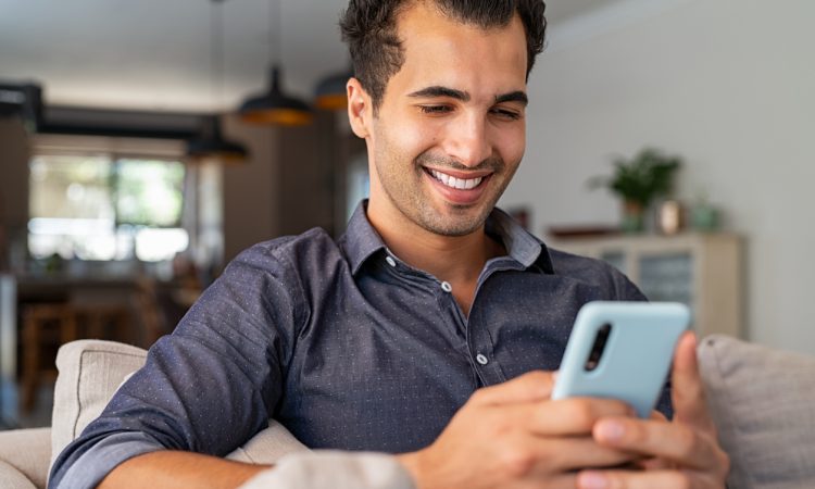 Cheerful businessman using smartphone while sitting on sofa at home.