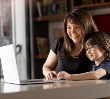 Mother and boy studying with laptop in home.