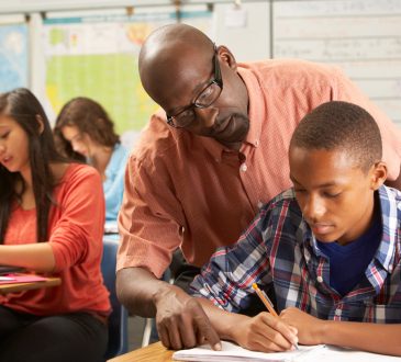 teacher helping pre-teen student in classroom