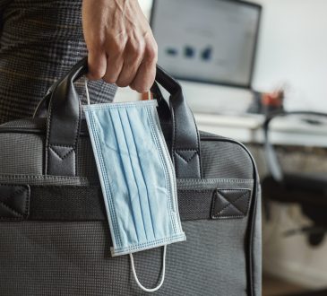 closeup of a young man in an office holding a briefcase and a surgical mask in his hand