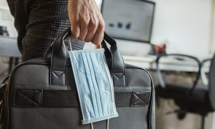closeup of a young man in an office holding a briefcase and a surgical mask in his hand
