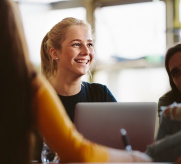Female student sitting amongst classmates and smiling in lecture room.